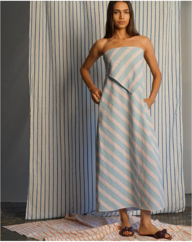 Woman wearing a strapless dress with vertical stripes in front of a striped curtain.